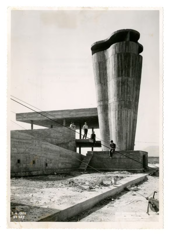 A vintage photograph dated 1950 showing several men standing casually atop a raw concrete modernist roof structure with a tall, curved ventilation tower. They overlook the landscape with a relaxed, possessive stance, evoking the "intoxicating confidence" of a people claiming their city.