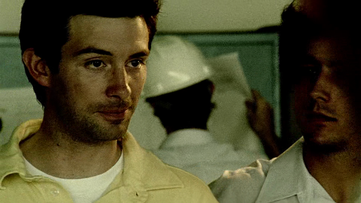 A wide shot of a vast warehouse where Aaron stands directing a group of workers constructing a colossal metal frame.