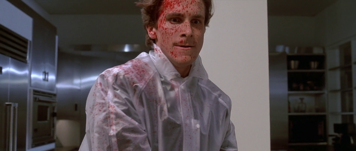 A still of Patrick Bateman from the film American Psycho, depicted with blood on his face and wearing a translucent rain poncho.